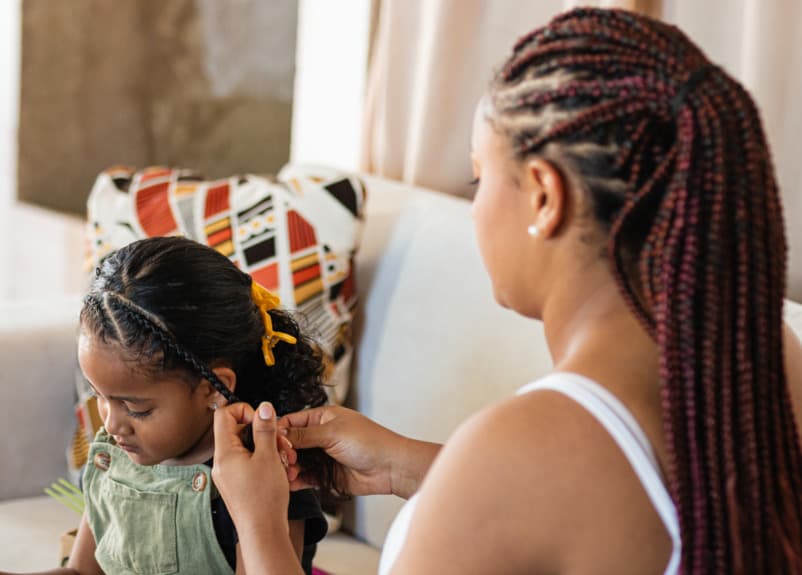 A professional braiding a child's hair at home